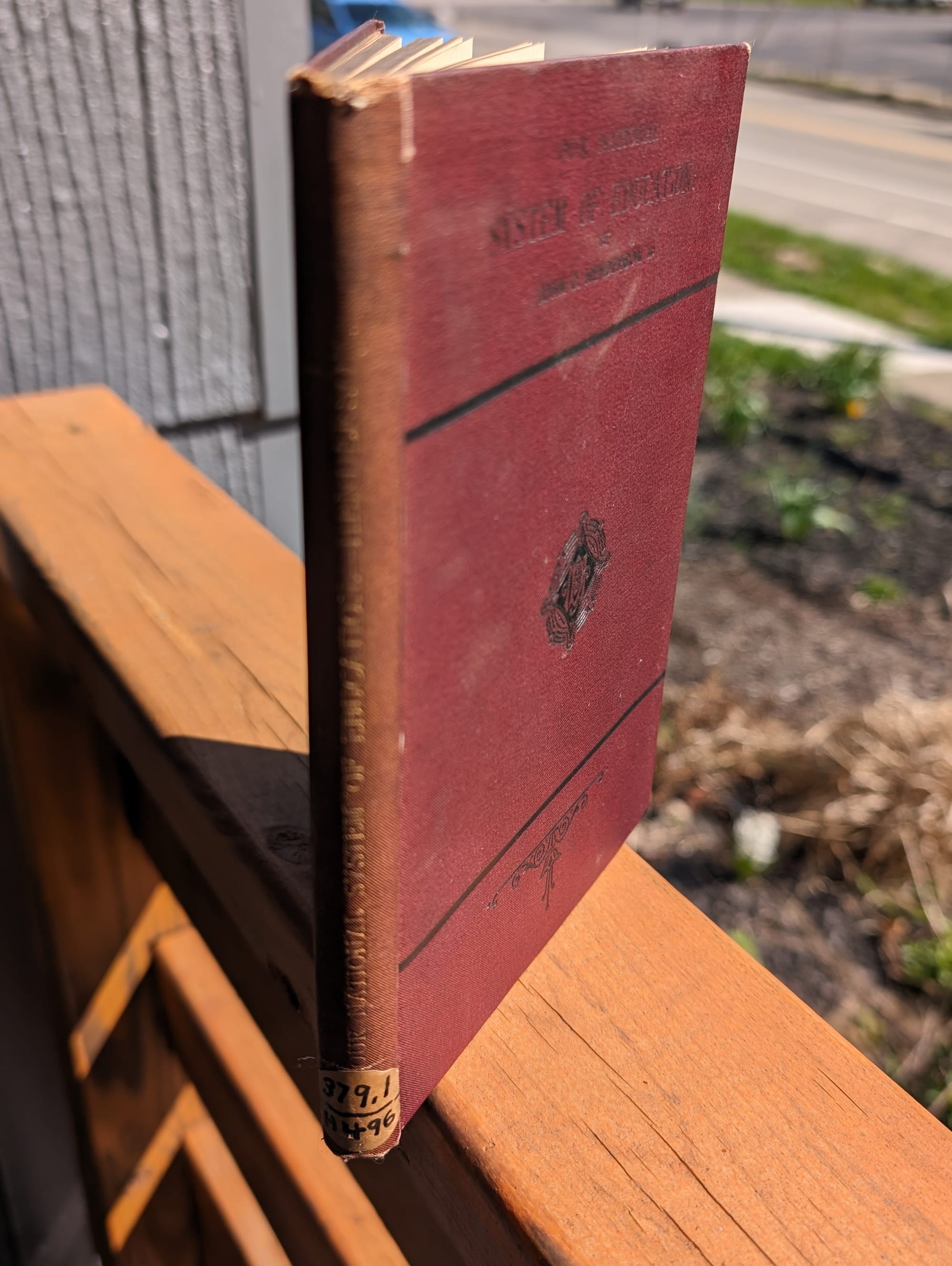 Photograph of Essay by Henderson. The book is sitting on a porch railing. There is a sticker that reads 379.1 on the spine.